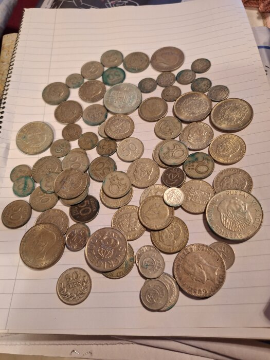 Gamla svenska mynt från tidigt 1900-tal, inklusive 2- och 5-kronor samt 25-öringar, utspridda på ett anteckningsblock.