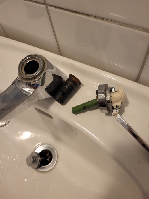 En demonterad köksblandare ligger på en vit diskho med delar bredvid; kranhandtag, cylinder och packning syns.