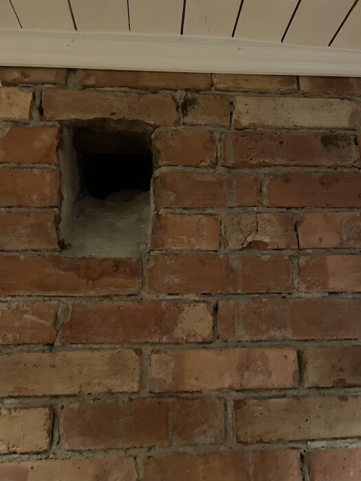 Tegelvägg med ett kvadratiskt hål nära taket, övervägs för installation av vedspis i ett hus från 1948.