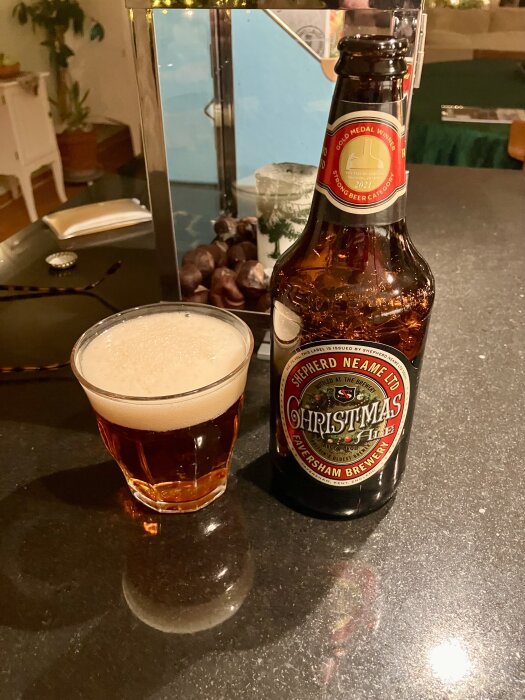 Flaska och glas med julöl på ett bord i ett hemtrevligt rum.