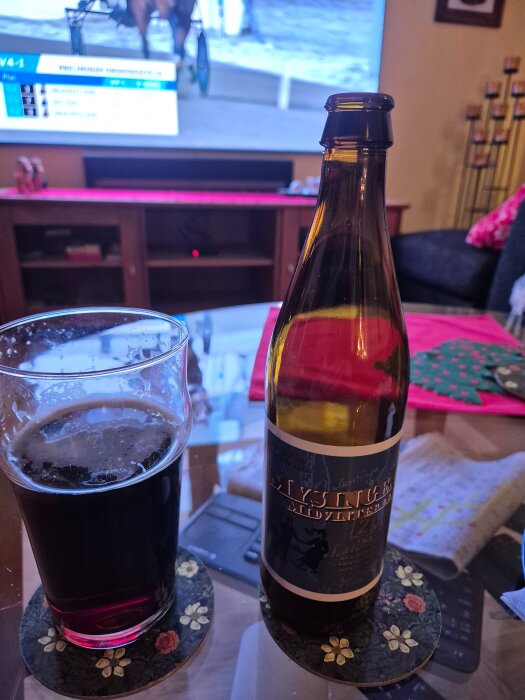 Flaska och glas med dryck på ett soffbord, TV i bakgrunden med travsändning.