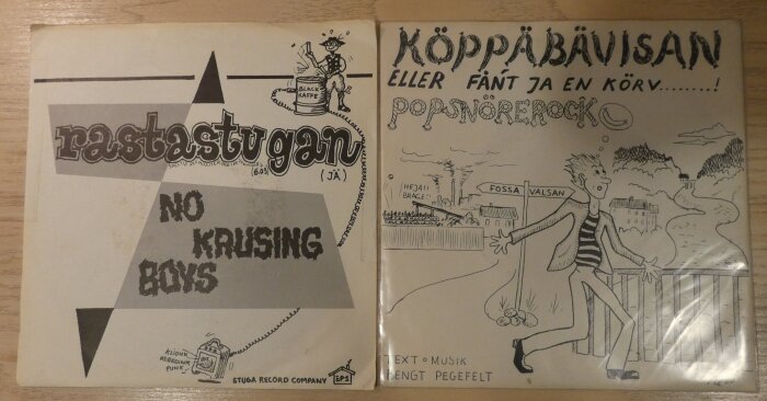 Två vinylskivor, "Rastastugan" av No Krusing Boys och "Köppäbävisan" av Popsnörock, med tecknad omslagskonst.