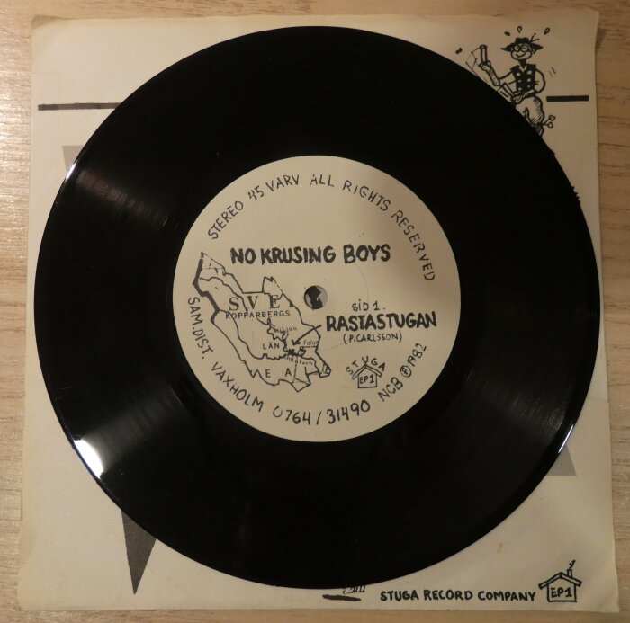 Svart vinylskiva med etikett som visar "No Krusing Boys" och låten "Rastastugan". Skivan ligger på ett skivomslag med enkel teckning.