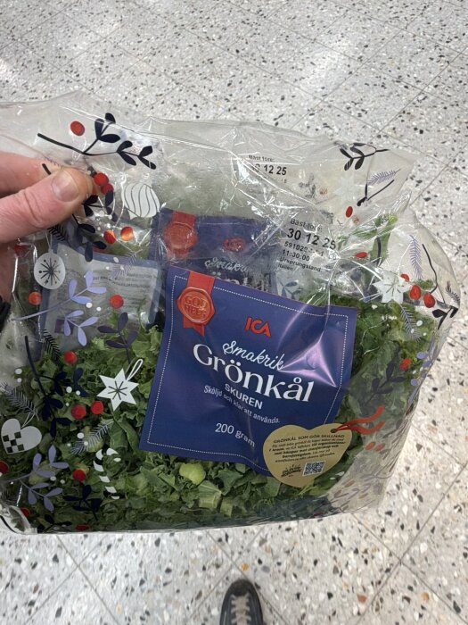 En hand håller en påse med skuren grönkål från ICA, dekorerad med julmotiv.