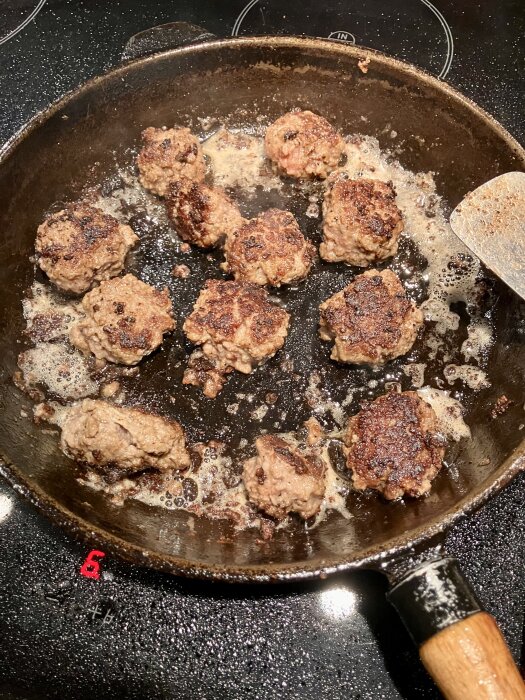 Köttbullar steks i en stekpanna på spishäll.
