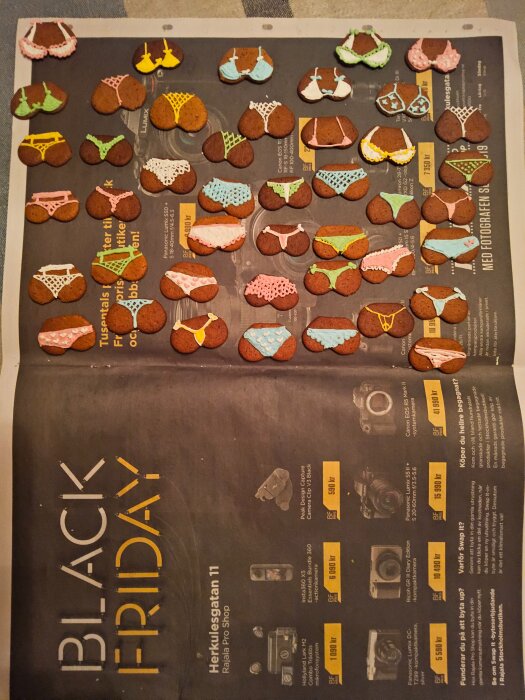 Pepparkakor dekorerade med glasyr i form av olika underkläder ligger på ett papper med Black Friday-annons i bakgrunden.