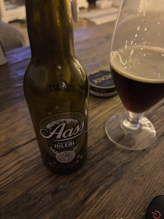 Flaska med Aass vel lager juleöl och glas på träbord.