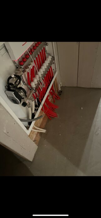 Vattenfördelarskåp med röda och vita slangar, synliga rördelar och en pump, monterade felaktigt enligt beskrivningen i inlägget. Golvyta intill skåpet.