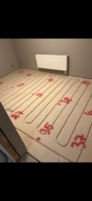 Golvet med flytspackel visar slingor för golvvärme och röda siffror, vilket tyder på pågående installation i ett renoveringsprojekt.