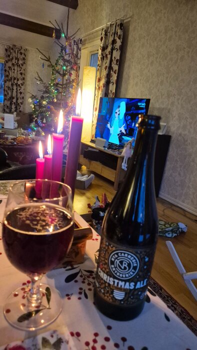 Julsmyckad interiör med tända ljus, julgran, julöl på bordet och TV som visar tecknat program.