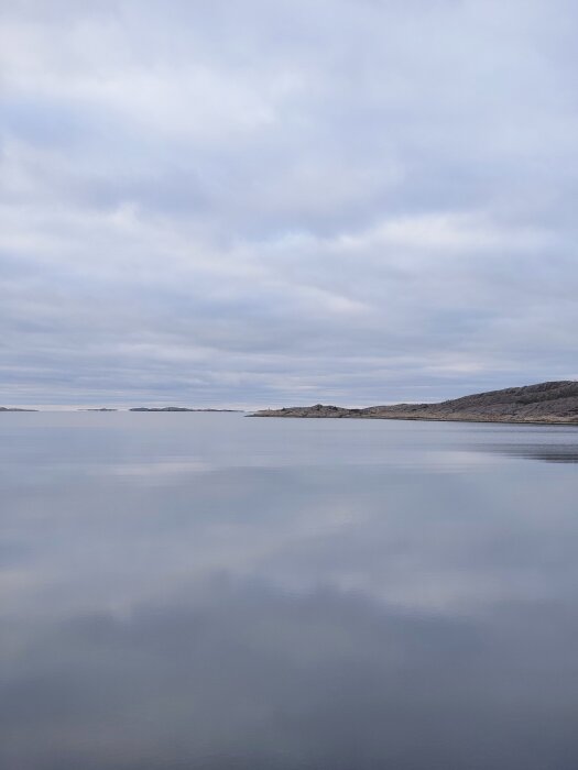 Gråmulen himmel över en lugn havsutsikt med låga klippor i horisonten, fotograferad under en julaftonspromenad.