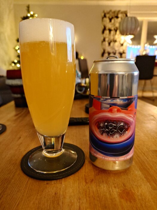 Ett glas Lumora Pale Ale bredvid en ölburk med konstnärlig etikett på ett bord i ett vardagsrum med julbelysning i bakgrunden.