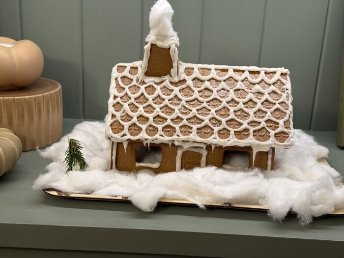 Pepparkakshus dekorerat med vit glasyr på ett vinterlandskap av bomull.