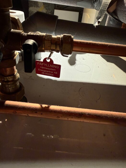 Ventil och kopparrör med en röd tagg märkt "Påfyllning Värmesystem Energipartner AB 08-802805".
