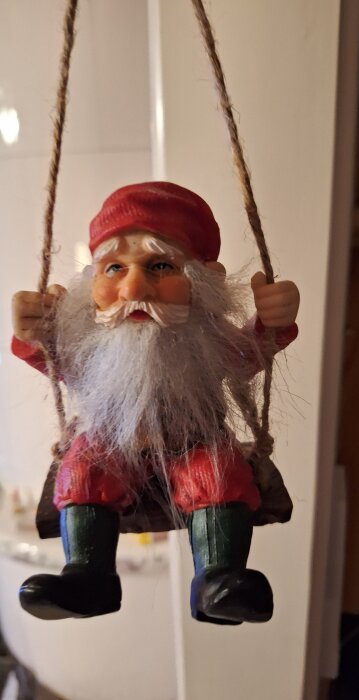 Tomtefigur med vitt skägg och röda kläder sitter på en gunga av rep.