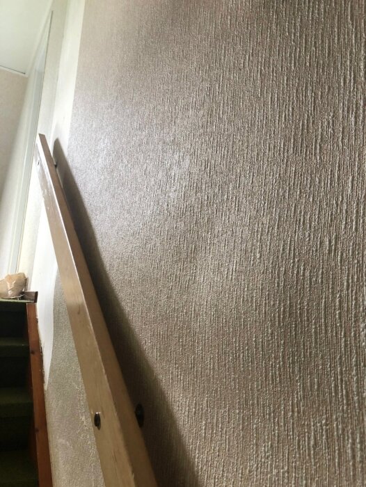 Vägg med texturerad tapet där det syns vågiga buktningar, troligen på grund av avstånd mellan spikrader som orsakar ojämn yta.