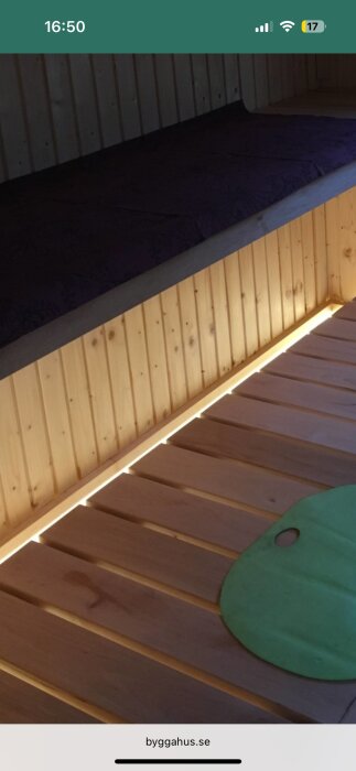 LED-strips monterade under en trähylla med ett grön oval föremål på träpanelen i en bastu eller relaxrum.