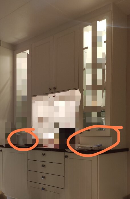 Köksskåp i allmogestil med höga socklar och vitrinskåp, två föremål markerade på bänkskivan framför skåpen.