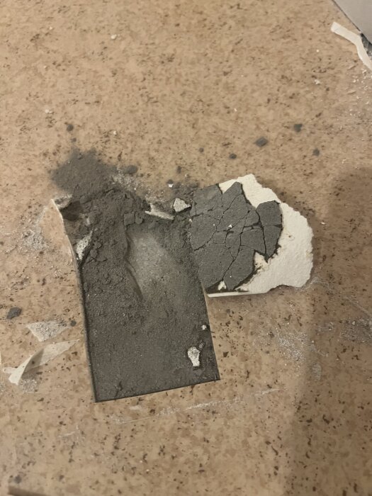 Sprucket material mellan plastmatta och betonggolv, visar lager av svart och vitt.