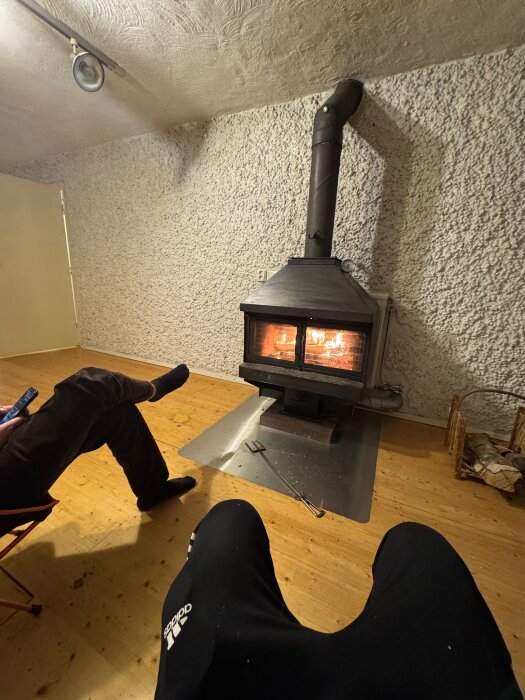 Källarvägg täckt med lekakulor bakom en braskamin, med två personer sittandes framför på trägolv.