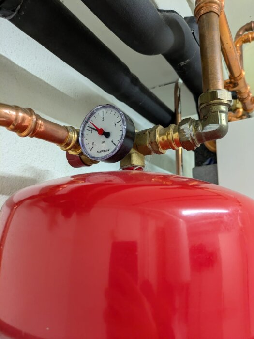 Manometer monterad på kopparrör ansluten till ett rött expansionskärl i en bygginstallation. Trycket visas på mätaren.