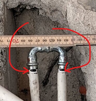 Två vita rör med svarta markeringar kopplade med metallfäste, röd markering och tumstock i bakgrunden.