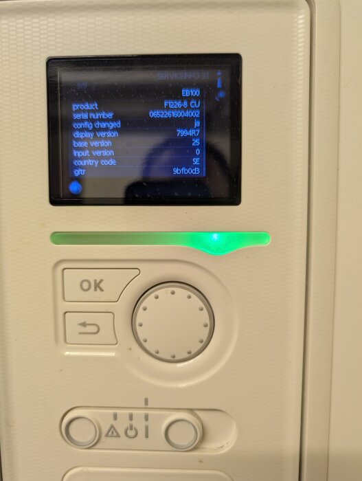 Kontrollpanel med display och knappar, visar serviceinformation för EB100 med serienummer och versioner, omgiven av vit ram och grönt ljus.