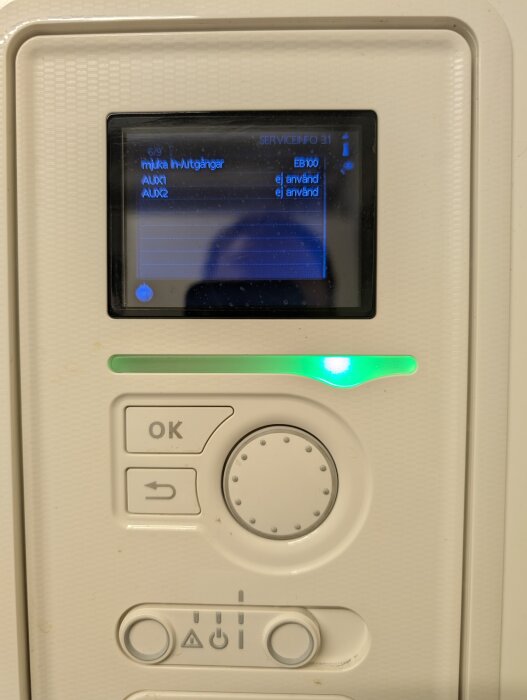 Kontrollpanel för värmesystem med skärm som visar menyval och knappar för inställningar, med en grön indikatorlampa som lyser.
