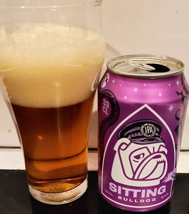 Ett glas IPA med skum ovanpå bredvid en lila burk öl märkt "Sitting Bulldog".