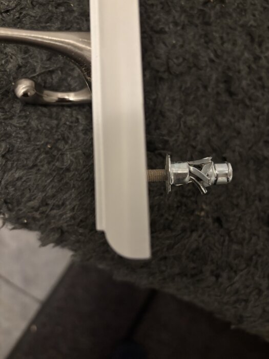 Mollyplugg med kroklist där pluggen är delvis utdragen och deformerad efter försök att montera den i väggen.