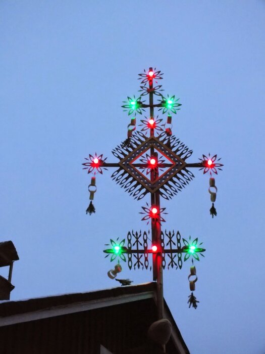 Julkors på ett tak med röda och gröna lampor, dekorerat med traditionella mönster mot en blå himmel.