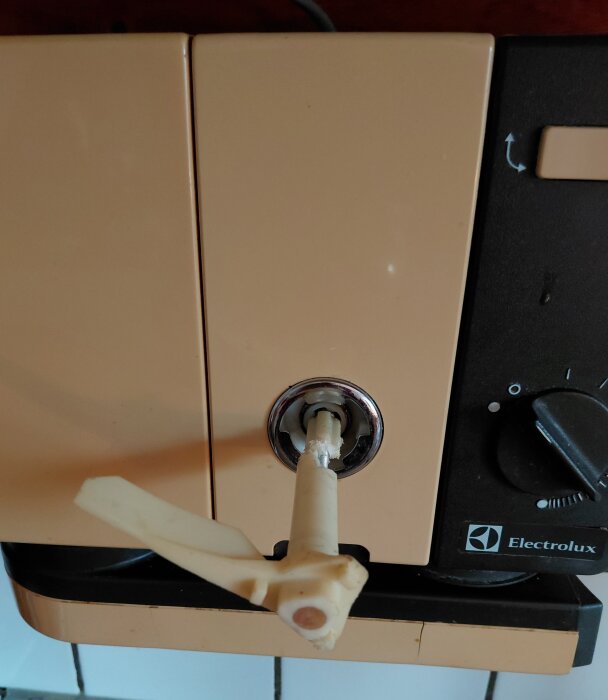 Närbild på en beige och svart Electrolux köksmaskin med en trasig plastvinge på en väggmonterad enhet.