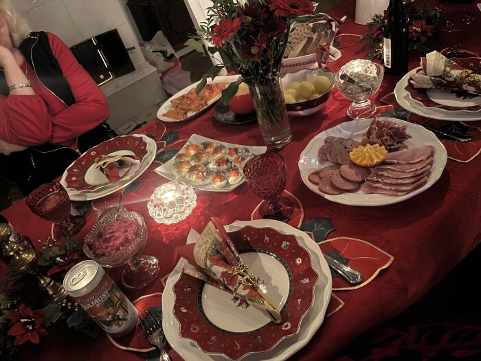 Julbord med tallrikar av pålägg, ägghalvor, rödbetssallad, och dukning med röda servetter. Stämningsfull belysning och blommor på bordet.