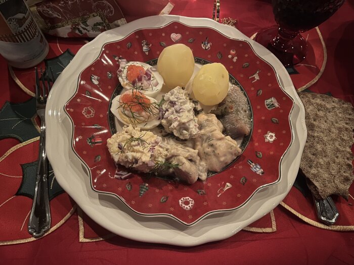 Jultallrik med ägghalvor, potatis, sill, gubbröra och hårt bröd på röd tallrik med julmotiv, dukad på julduk.