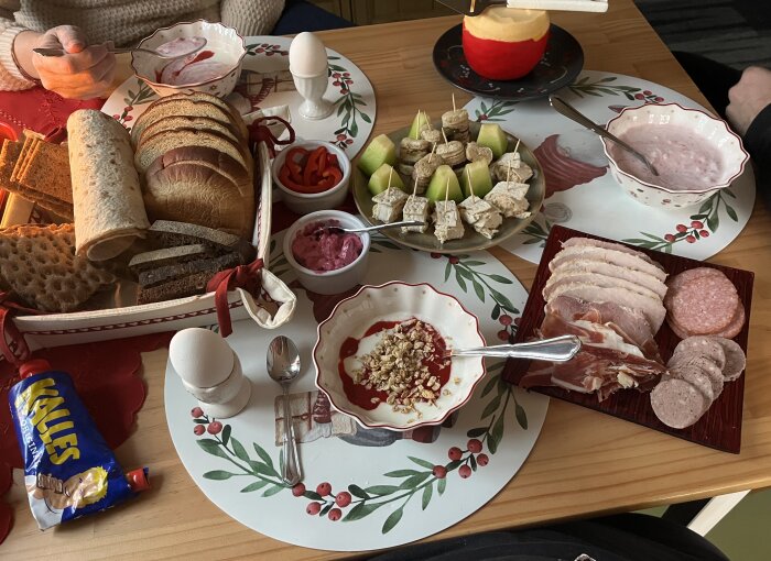 Frukostbord med bröd, kallskuret, kaviar, ägg, fruktspett, yoghurt med granola och skålar med rödbetssallad och skivad paprika.