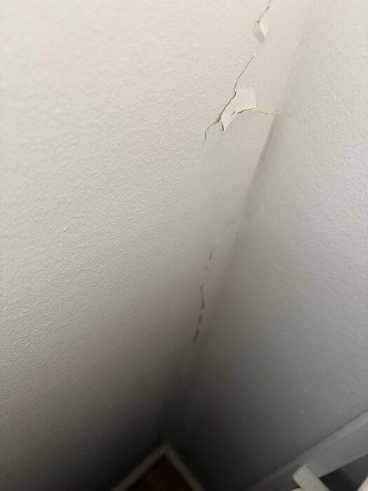 Sprickor i väggfärg i ett hörn av ett rum.