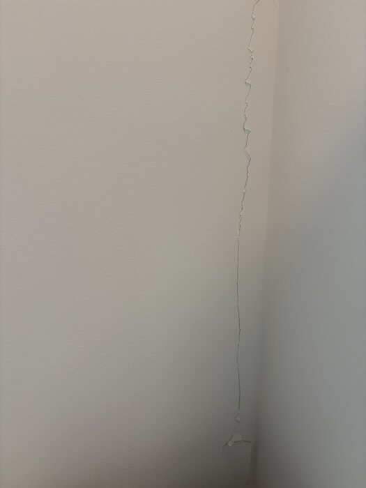 Spricka i ett hörn på en innervägg med avflagande färg, som indikerar potentiella strukturella problem.