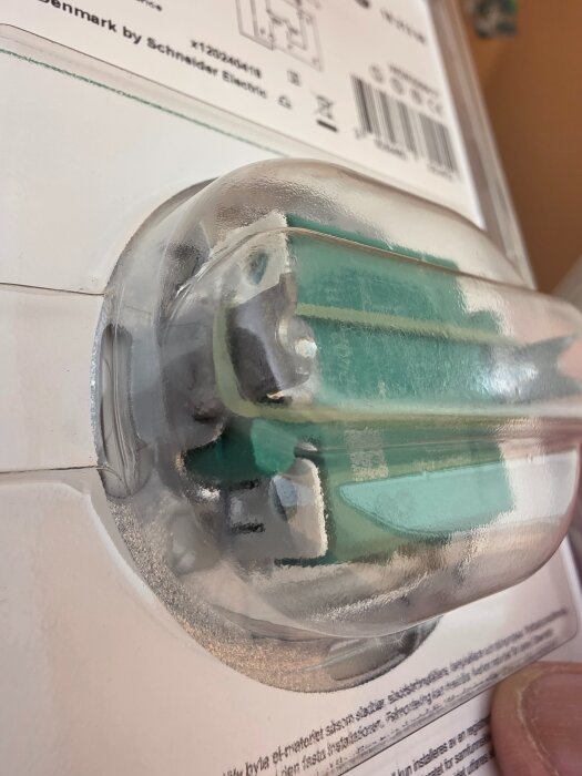 Närbild av en genomskinlig plastdel med synliga gröna och vita komponenter, del av en plastförpackning eller teknisk utrustning.