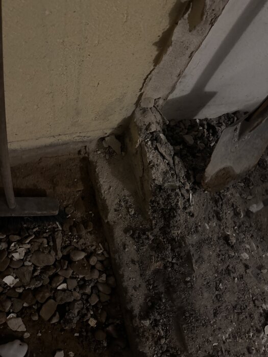 Betongfundament inomhus, delvis bortbilad. Omgivet av småsten och verktyg, syns mot en vägg i lättbetong.