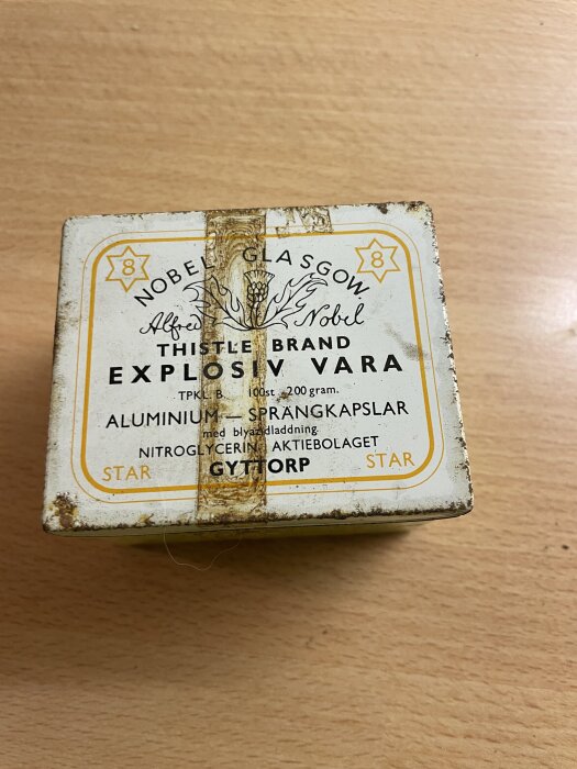 Aluminiumask med etikett för explosiva varor, märkt med Nobel och Gyttorp, synligt tejprester på lockets yta.