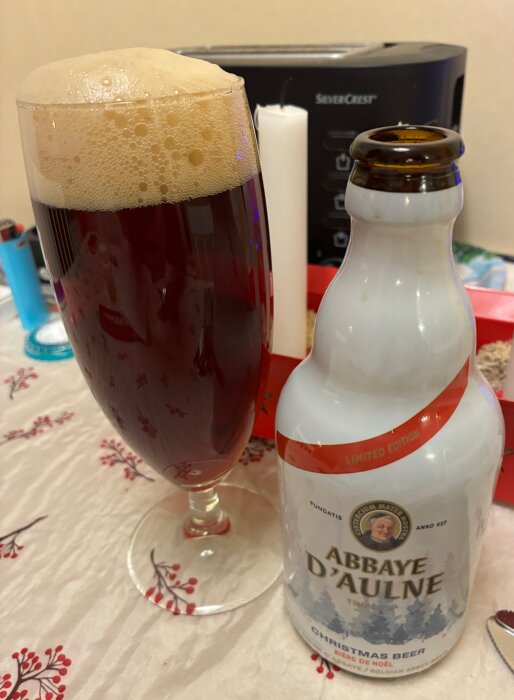 Mörk öl i glas och en flaska Abbaye D'Aulne Christmas Beer på ett bord med juldukar.