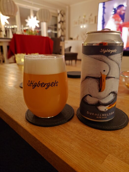 Ett glas fyllt med öl och en ölburk märkt "DubbelNelson" står på ett bord i ett inomhusmiljö med juldekorationer i bakgrunden.