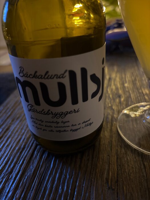 Flaska från Bäckalund Mullsjo Gårdsbryggeri på bord, intill ett glas.