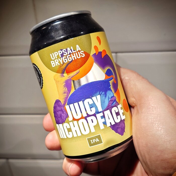 En hand håller en burk Juicy McHopface IPA från Uppsala Brygghus med färgglad etikett.