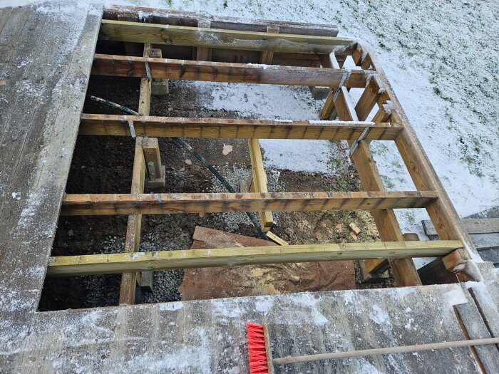 Byggkonstruktion av trä med plintar och bjälkar på en byggarbetsplats för en stuga, delvis täckt av snö.