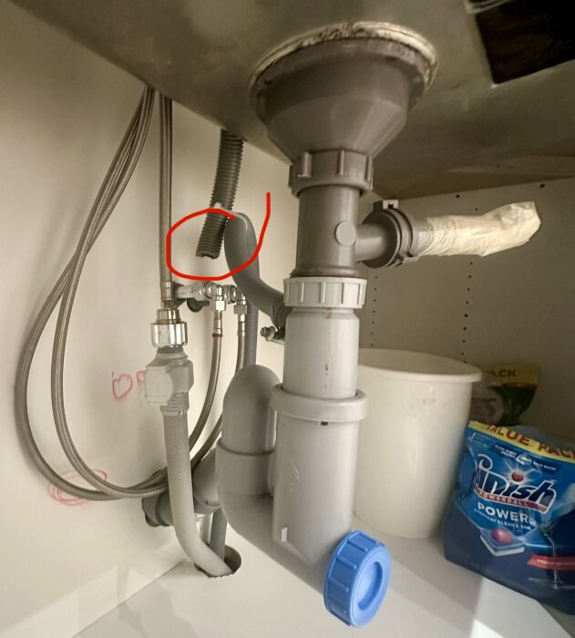Under köksbänken med avloppsrör där ett avbrutet rör tejpats; röd ring markerar ohållbar koppling.