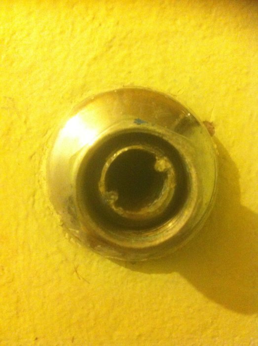 Rörkoppling i metall med synlig invändig och utvändig gänga monterad i en gul vägg, potentiellt gammalt eller skört material.