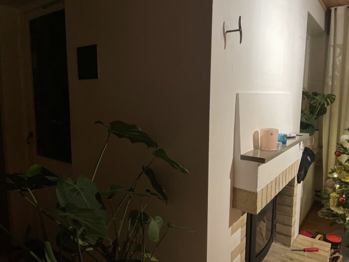 Öppen spis i vardagsrum med väggmonterat gammalt spjällhandtag som dekorativ detalj, sotlucka till vänster och julgran i höger hörn.