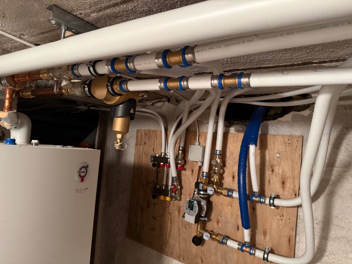 Golvvärmeanläggning med kopplingar och fördelare installerad på träpanel, visar rörsystem med olika ventiler och röranslutningar.