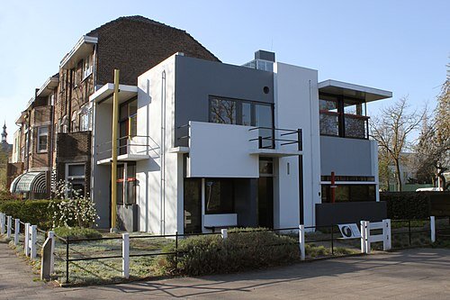 Vit och grå modernistisk byggnad med platta tak, stora fönster och geometriska former längs en gata, ofta presenterad som ett exempel på modernism.